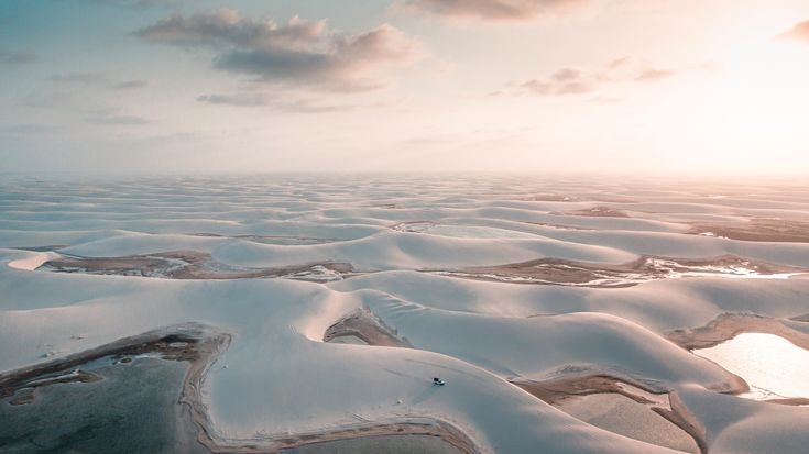 an aerial view of snow covered hills and lakes at sunset or sunrise with clouds in the sky