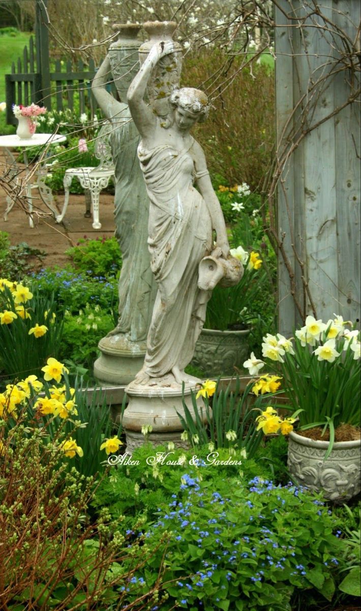 a statue in the middle of a garden surrounded by flowers and plants with text overlay