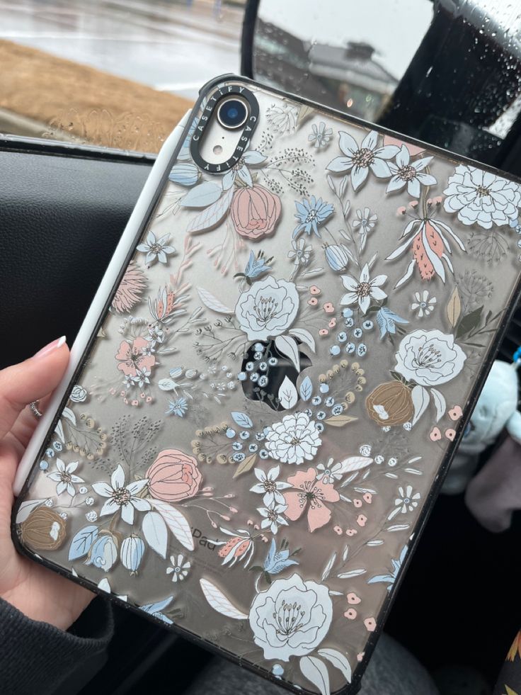 a person holding up an iphone case with flowers on it in front of a car