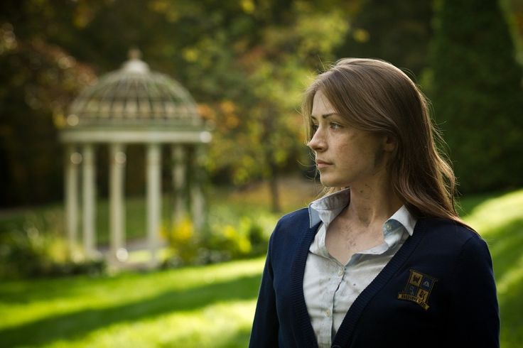 a woman standing in front of a gazebo looking off into the distance with trees and grass behind her