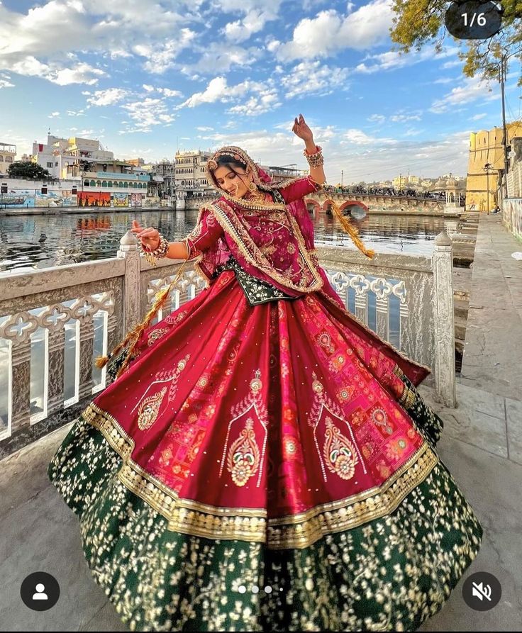 a woman in a red and green dress standing on a bridge with her arms outstretched