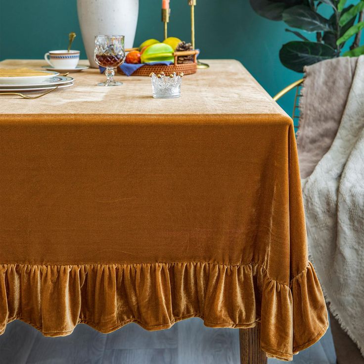 the table is set with an orange cloth and fruit on it, along with two white vases