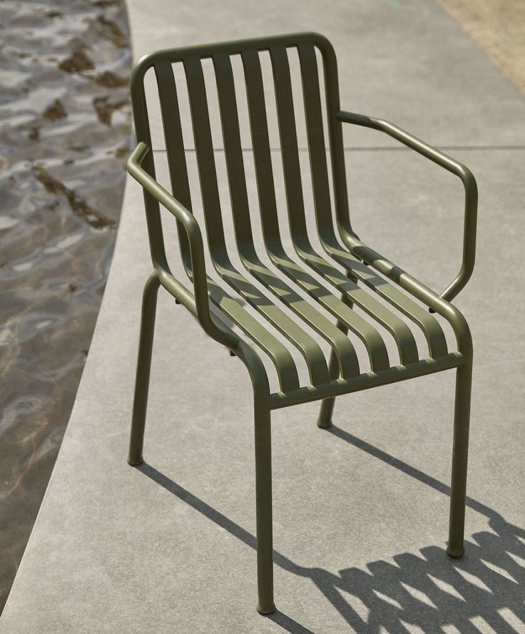 a green chair sitting on top of a cement ground next to a body of water