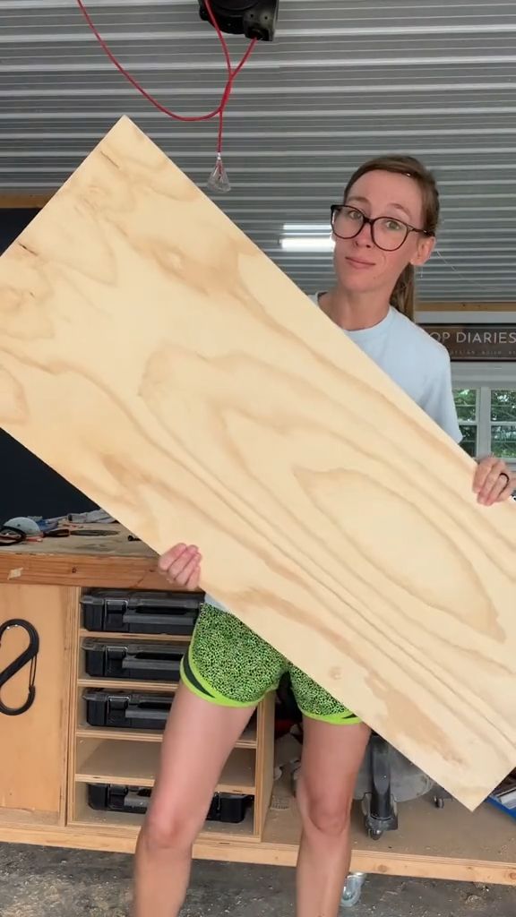 a woman holding a large piece of wood in front of her face while wearing green shorts