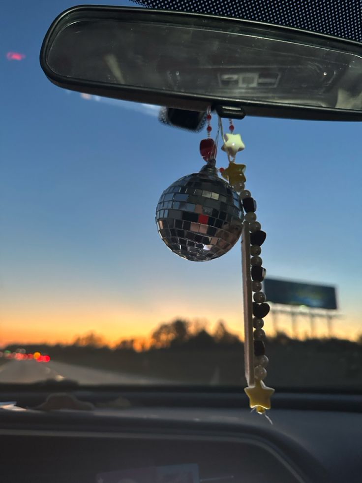 a disco ball hanging from the side of a car window at sunset or dawn with stars and beads attached to it