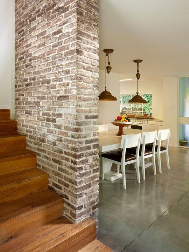 a dining room table and chairs next to a brick wall in a house with stairs