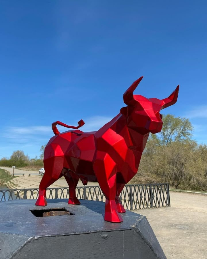 a red sculpture of a bull on top of a cement slab