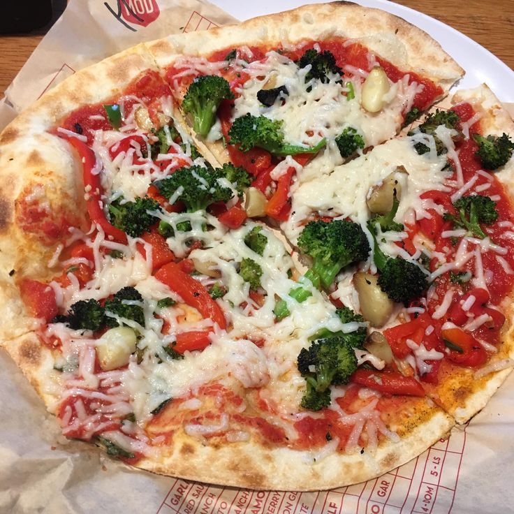 a pizza sitting on top of a white plate covered in cheese and veggies