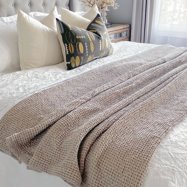 a bed with white linens and pillows on top of it next to a window