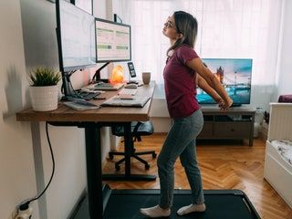 a woman standing on a treadmill in front of a computer desk with a monitor and keyboard