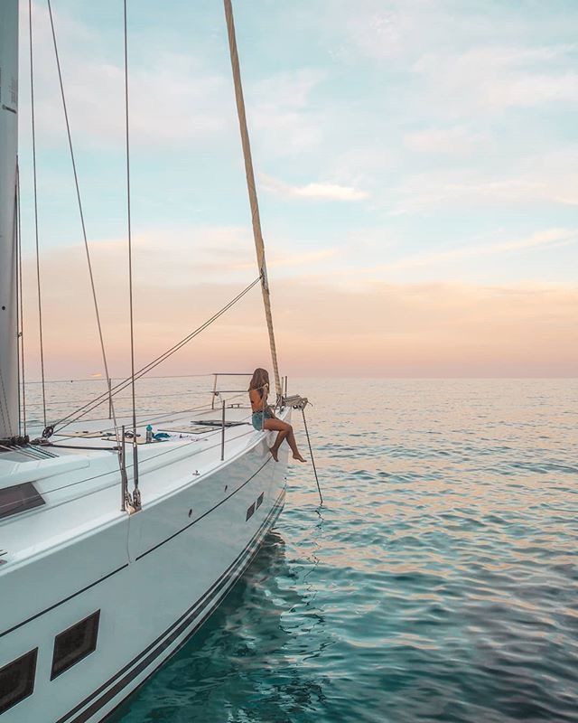 a man sitting on the bow of a sailboat in the ocean at sunset or sunrise