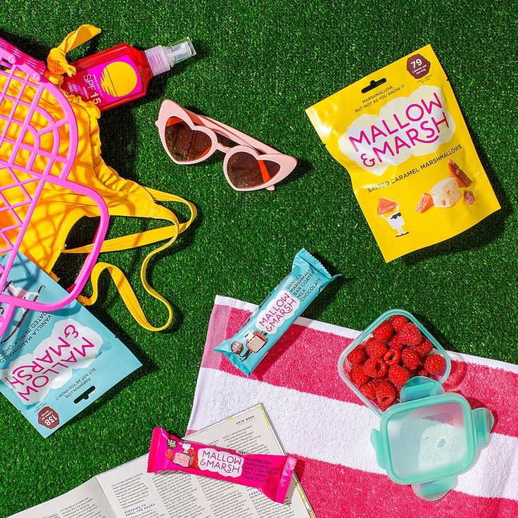 the contents of a beach bag laid out on green grass next to sunglasses, candy and other items