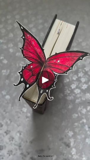 a red butterfly sitting on top of an open book with the pages folded down to look like it's flying