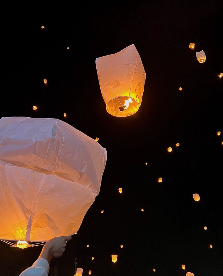 people releasing paper lanterns into the sky at night with bright lights in the dark background