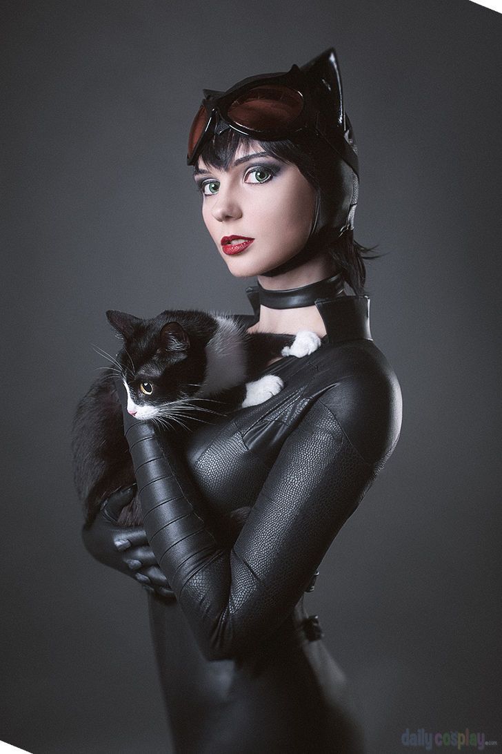 a woman in catwoman costume holding a black and white cat on her chest,