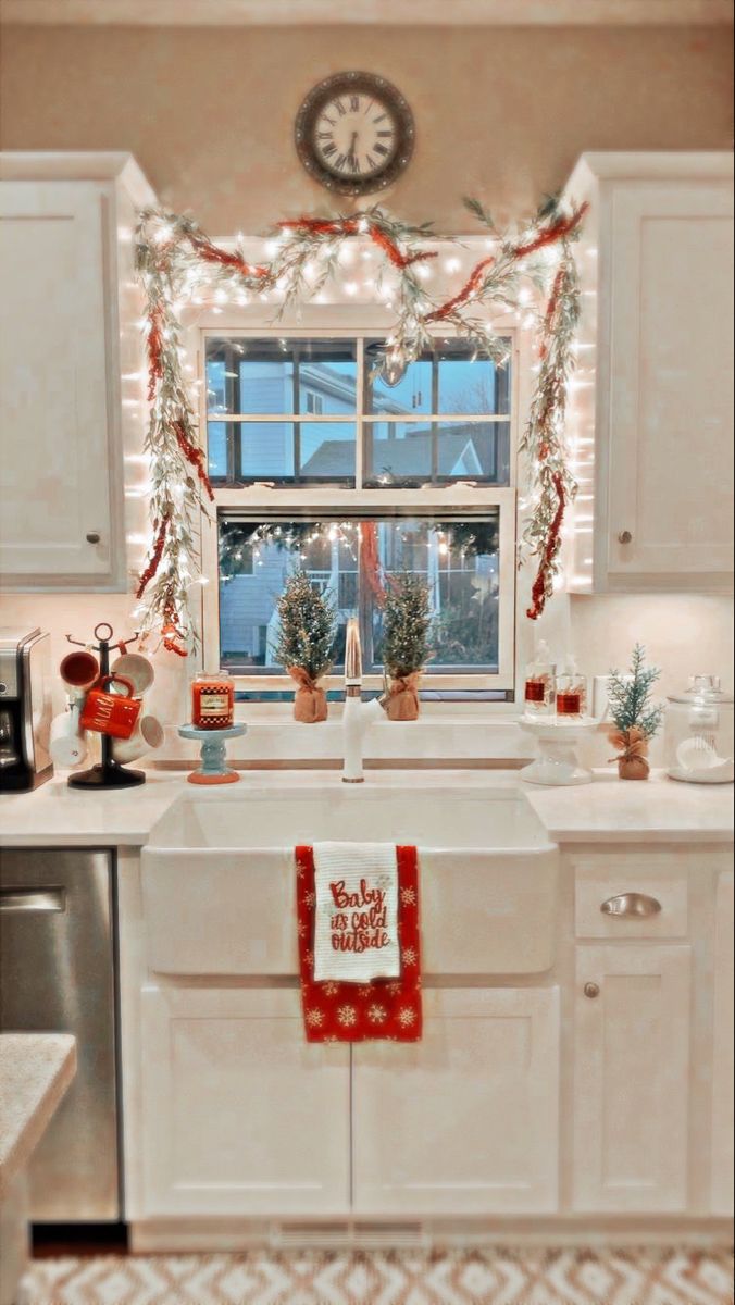 a kitchen decorated for christmas with lights and garland on the window sill above the sink