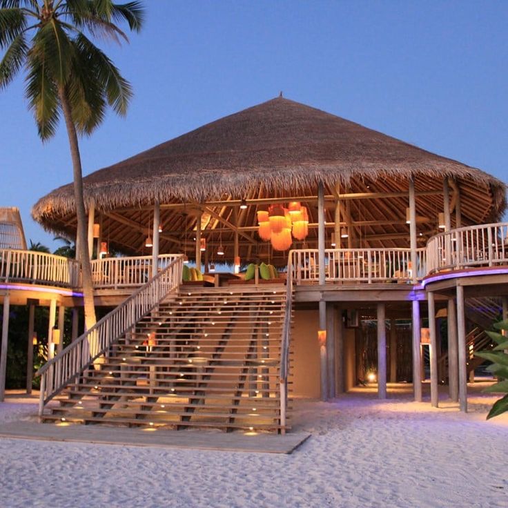 a beach side restaurant with stairs leading up to the roof and palm trees around it