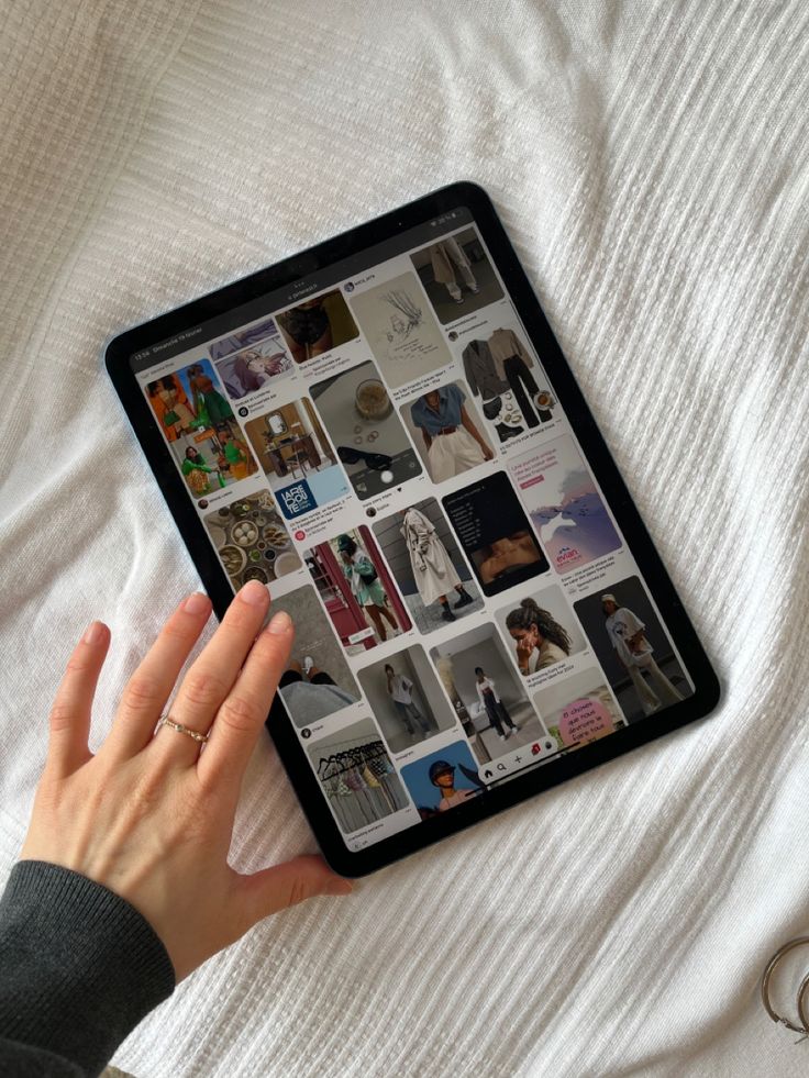 a person holding an ipad on top of a white bed covered in sheets and pillows