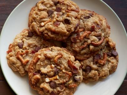 four chocolate chip cookies on a plate with pecans in the middle and one half eaten