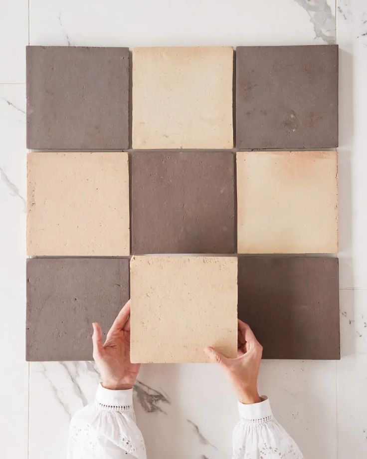 a person holding up a piece of cardboard with different colored squares on it in front of a marble wall