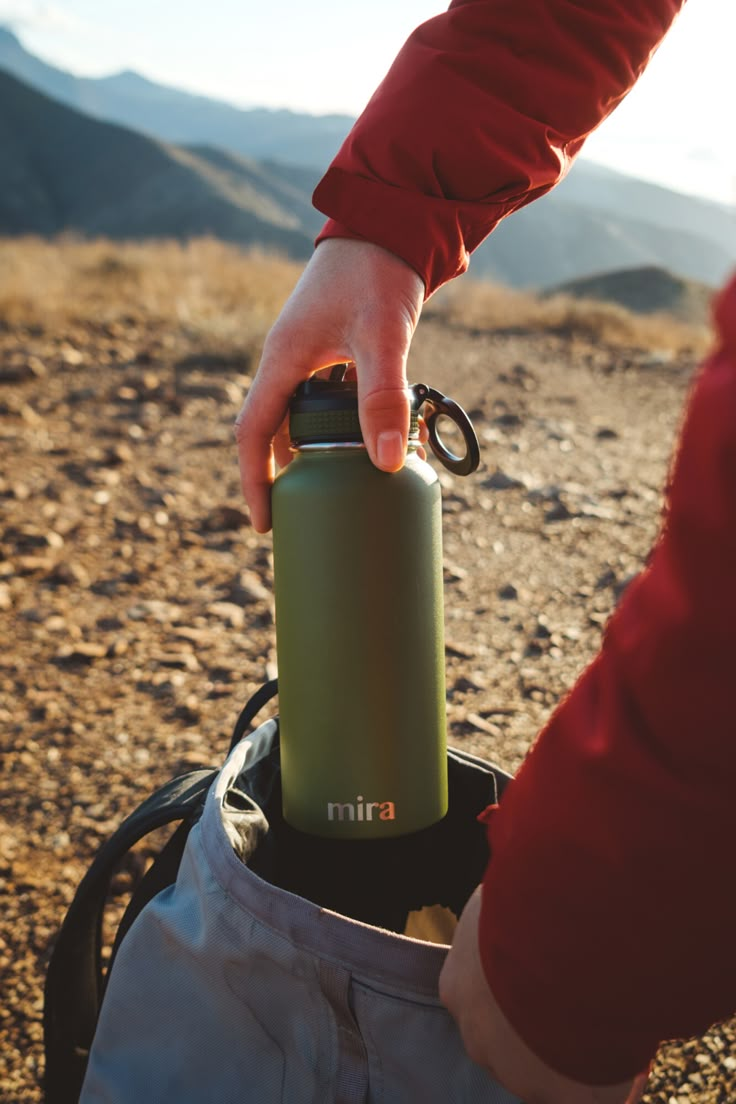 a person holding onto a green water bottle in the dirt with mountains in the background