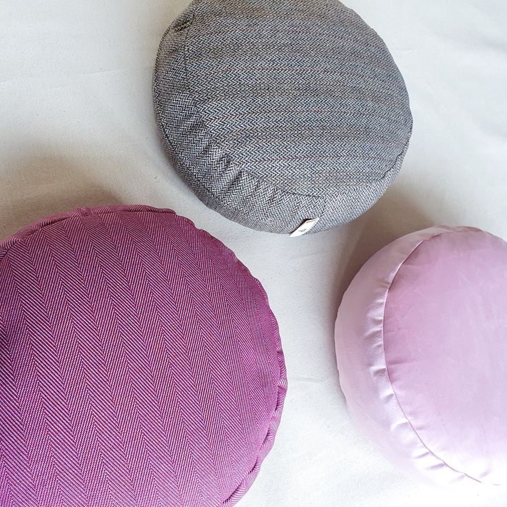 three different colored pillows sitting on top of a white bed sheet next to each other