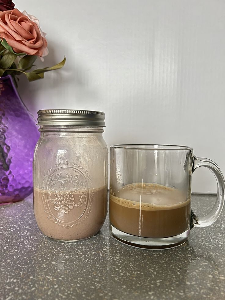 there is a glass mug with liquid in it next to a vase