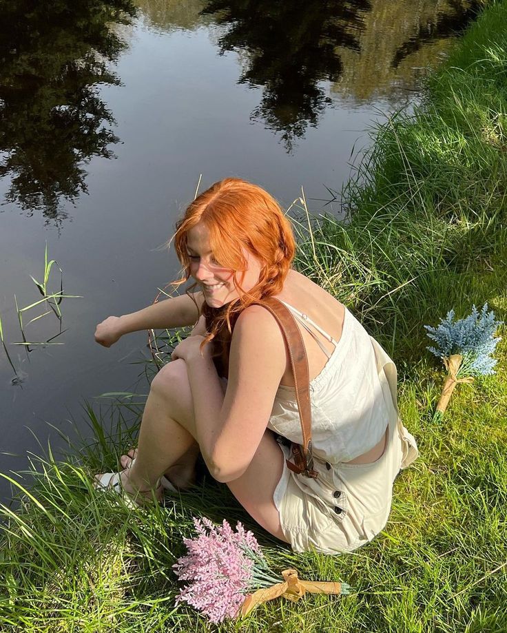 a woman kneeling down next to a body of water