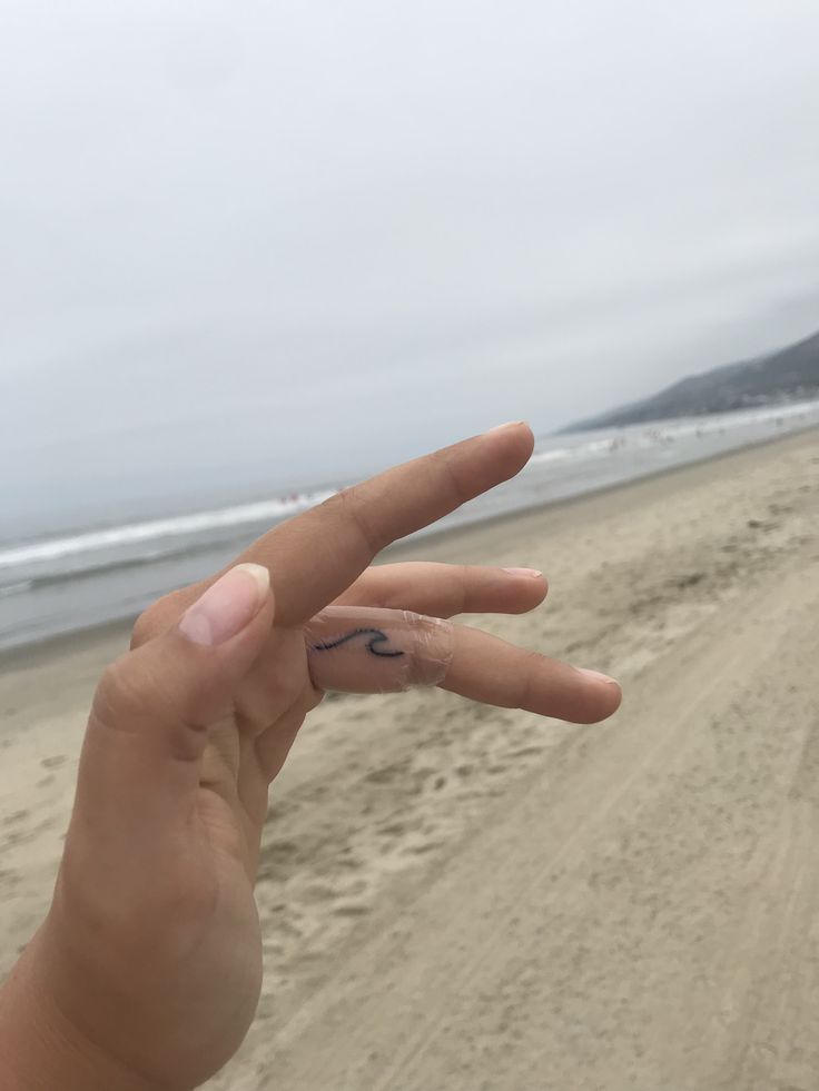 a person's hand with two fingers in the air on a sandy beach near the ocean