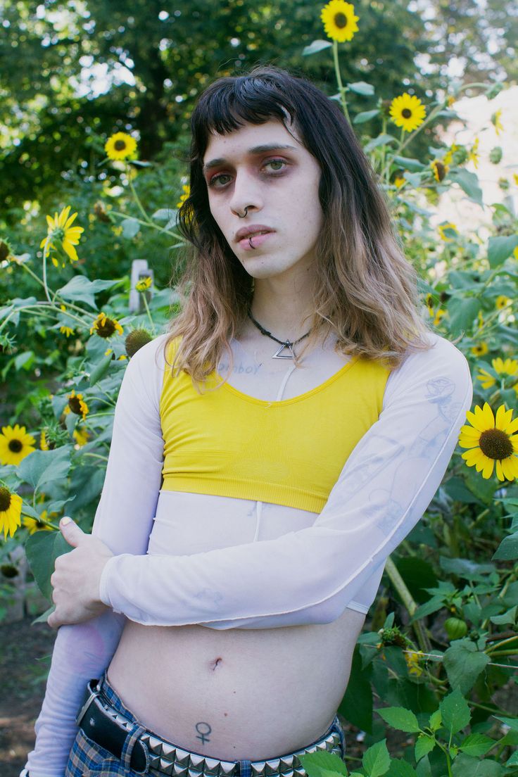 a woman with long hair standing in front of sunflowers wearing a yellow crop top