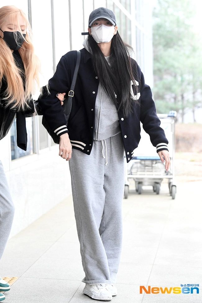 two women walking down the street wearing face masks on their faces as they both wear grey sweatpants and black jackets