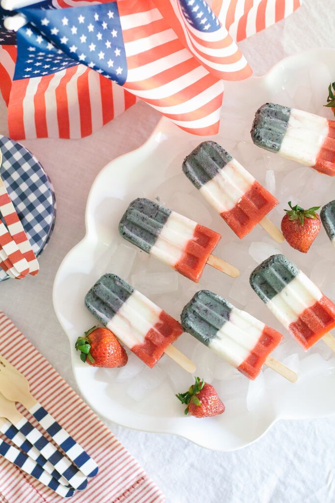 american flag popsicles on a plate with strawberries and an american flag napkin in the background