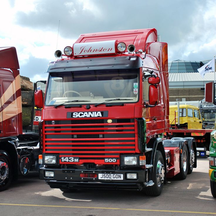 three semi trucks are lined up in a parking lot, one is red and the other is green