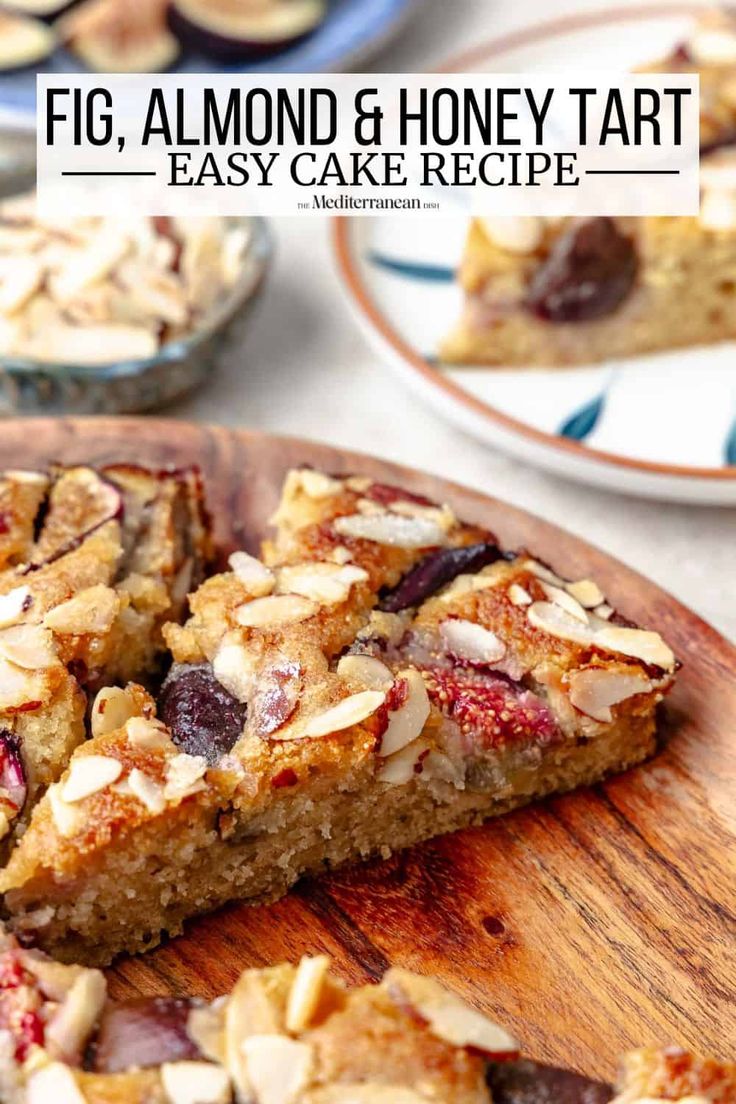 a wooden cutting board topped with slices of fruit and honey tart cake next to other desserts