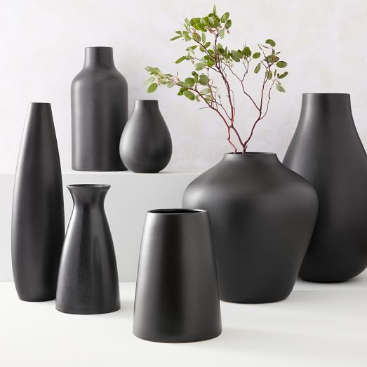 several black vases are lined up on a white table with a plant in the middle