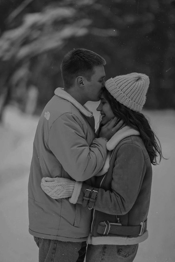 a man and woman standing next to each other on a snow covered road with trees in the background