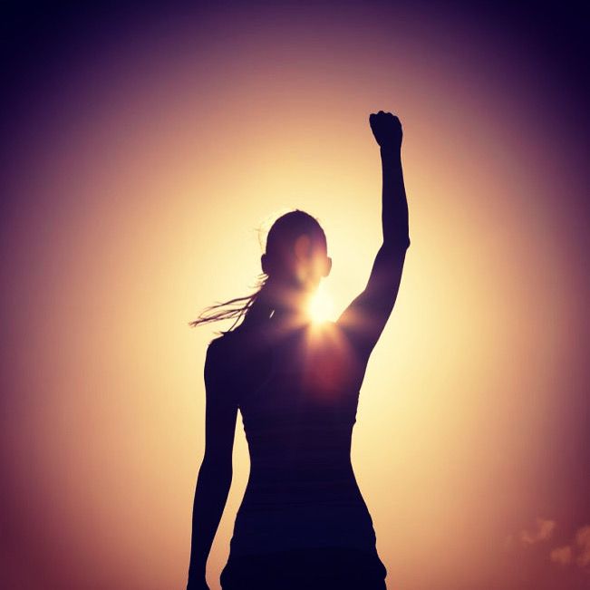 a woman raising her arms in the air at sunset