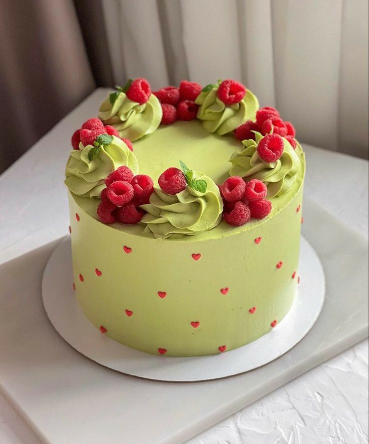 a yellow cake with raspberries and green icing on a white tablecloth