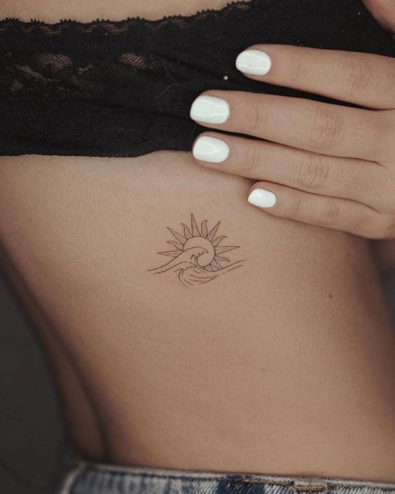 a woman's stomach with a small sun tattoo on her left side ribcage