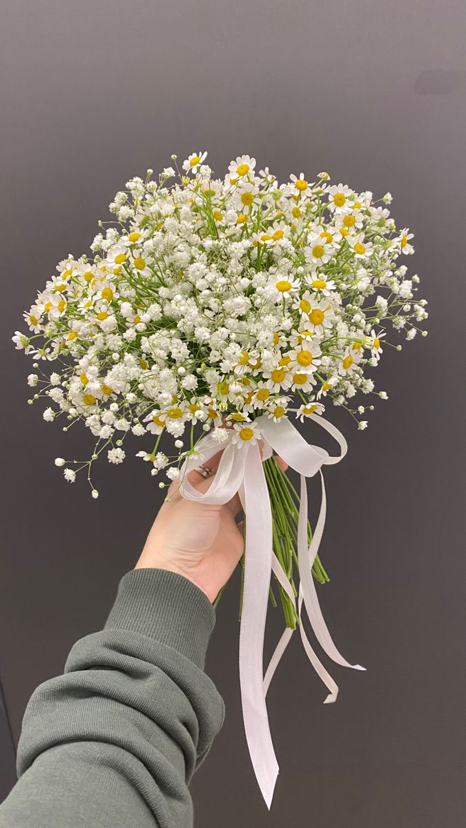 a person holding a bouquet of daisies with white ribbons on their wrist and hand