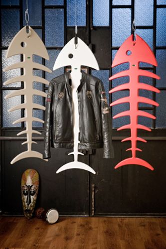 three metal fish hanging from hooks in front of a blue and black wall with a leather jacket on it