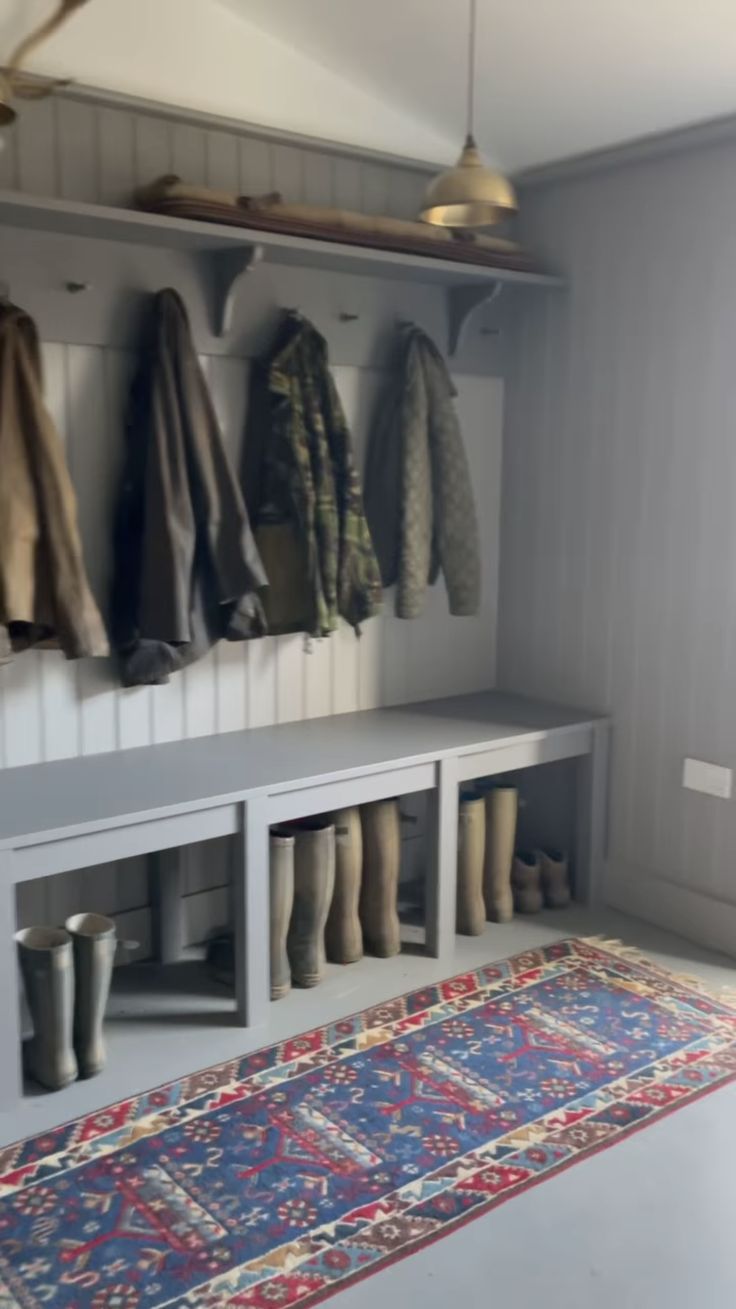 a room with several coats and boots hanging on the wall next to a blue rug