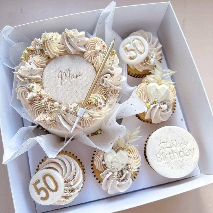 a box filled with lots of cupcakes covered in white frosting and gold decorations