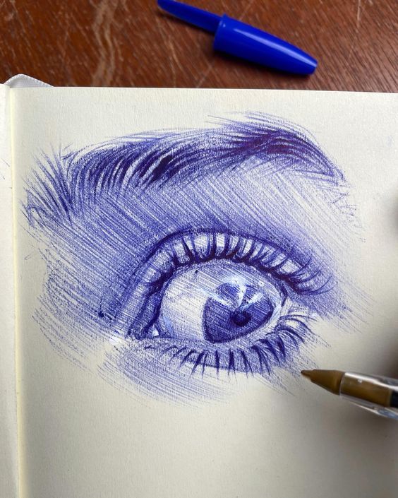 a pencil drawing of an eye with blue eyeshade and long eyelashes, on top of a piece of paper