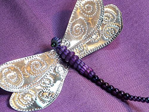 a purple and silver dragonfly brooch with beads on it's back end