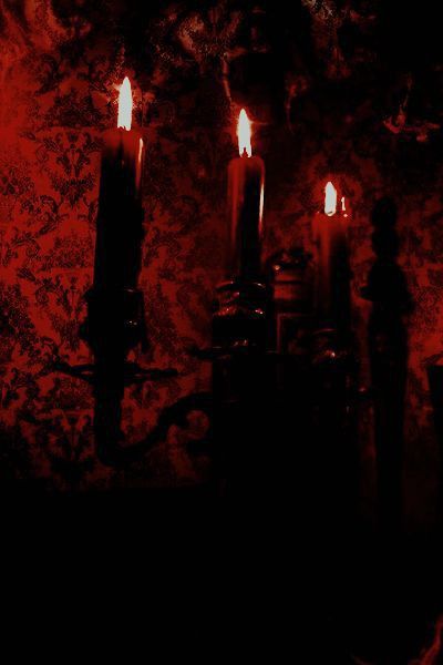 three lit candles in front of a red wall with black and white designs on it