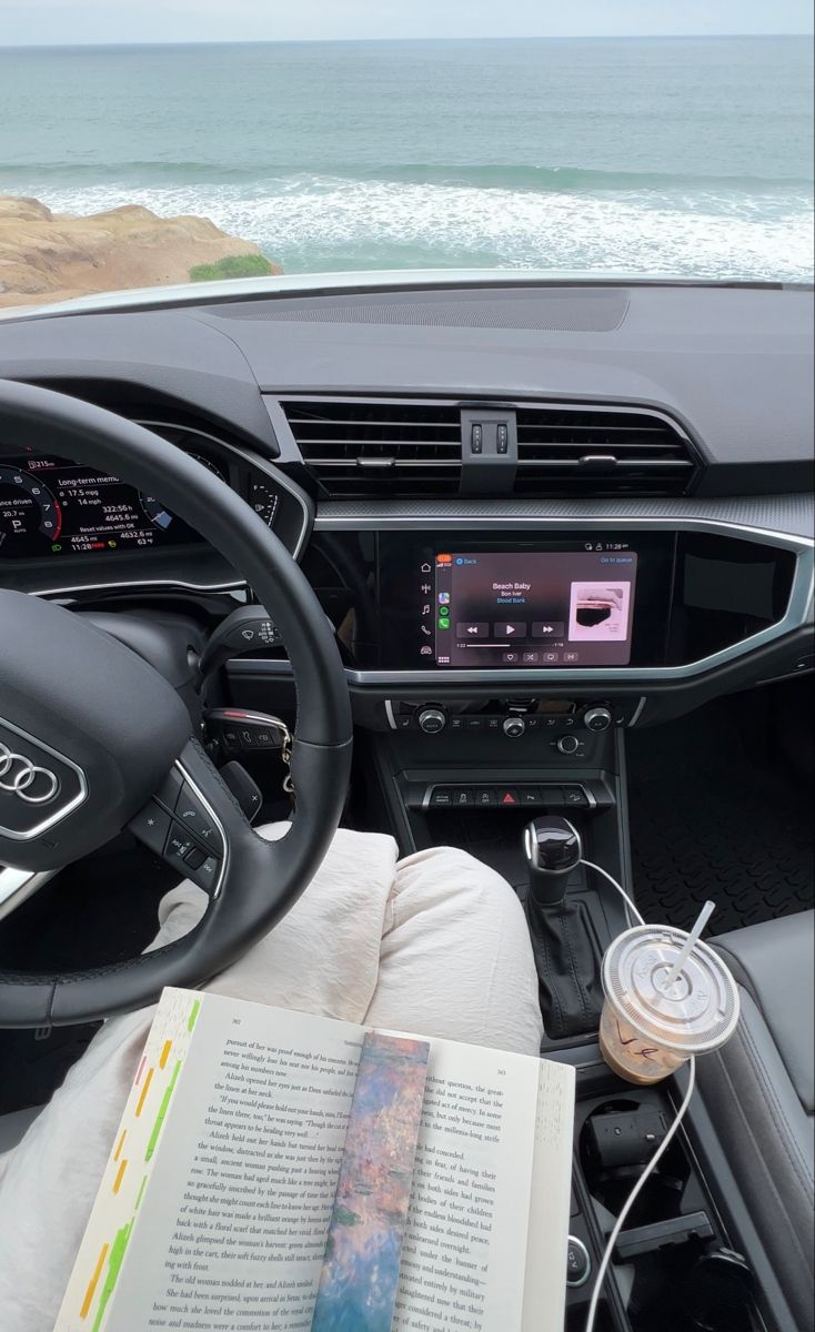 the interior of a car with an open book on the dashboard and ocean in the background