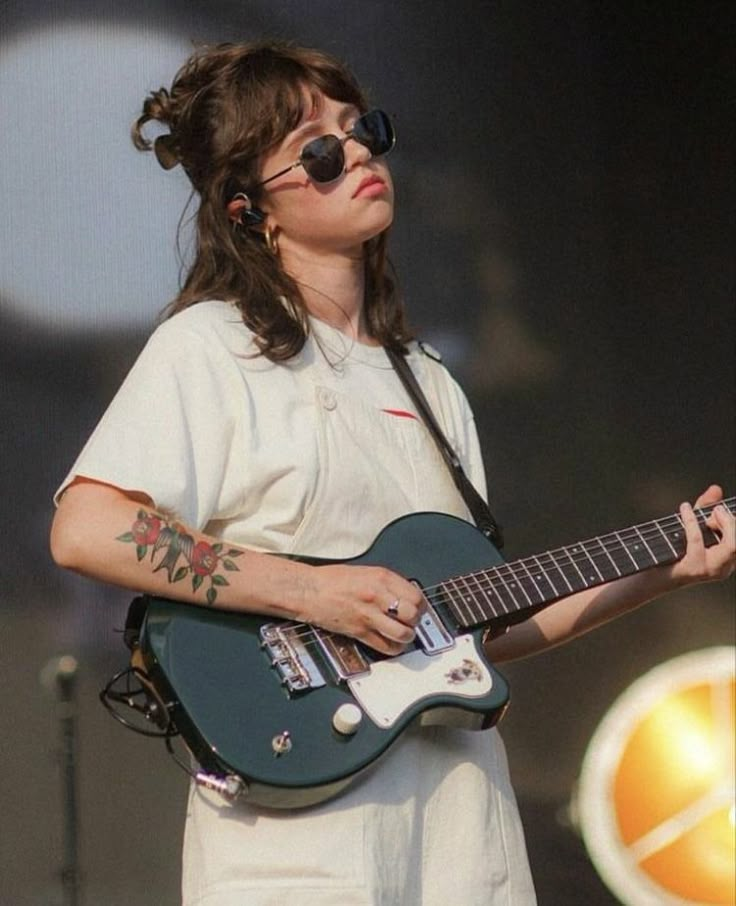 a woman holding a green guitar on top of a stage