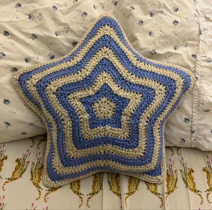 a crocheted blue and white star pillow sitting on top of a bed next to pillows