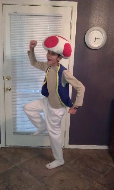 a young boy wearing a mushroom hat while standing in front of a door with his arms up